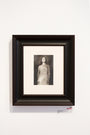 Framed black-and-white photograph titled Katie by Karla Ortiz, part of the chimerical exhibition, features a woman in a strapless dress looking upward. The frame is dark brown with an off-white mat, mounted on a plain white wall.