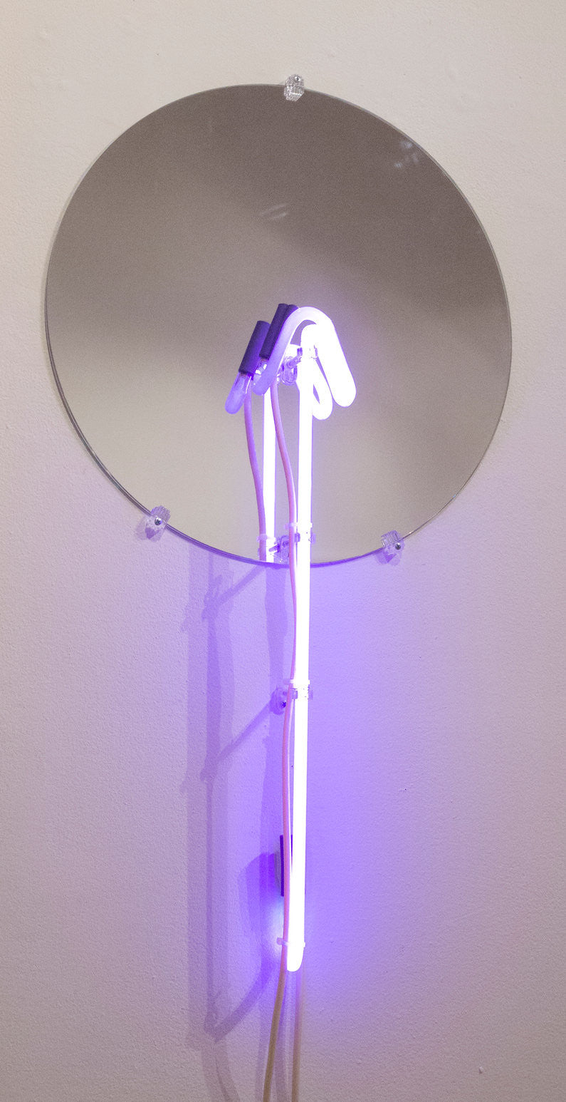 A round mirror on a white wall reflects the mesmerizing purple glow of Meryl Patakys glass neon art, featuring beautifully curved tubes.