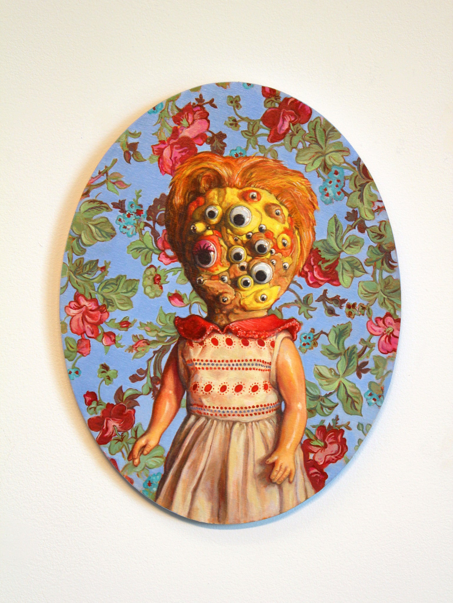 Allan Innmans oil on canvas showcases a multi-eyed doll with a red and white dress against a floral backdrop, creating an eerie, captivating effect. Now available for sale as art.