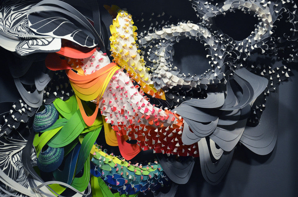 This abstract art installation, by Crystal Wagner, boasts layered swirling shapes in vibrant colors like yellow, orange, and green. Black, white, and gray elements intertwine within the 3D design for a dynamic textured visual display.
