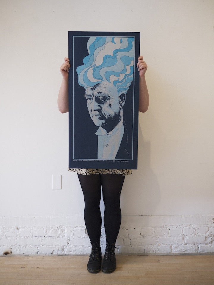 A person in black tights and shoes stands by a light wall, holding a large poster over their face. The poster displays a monochrome portrait with abstract blue and white hair on a dark background, reflecting Chuck Sperrys style.