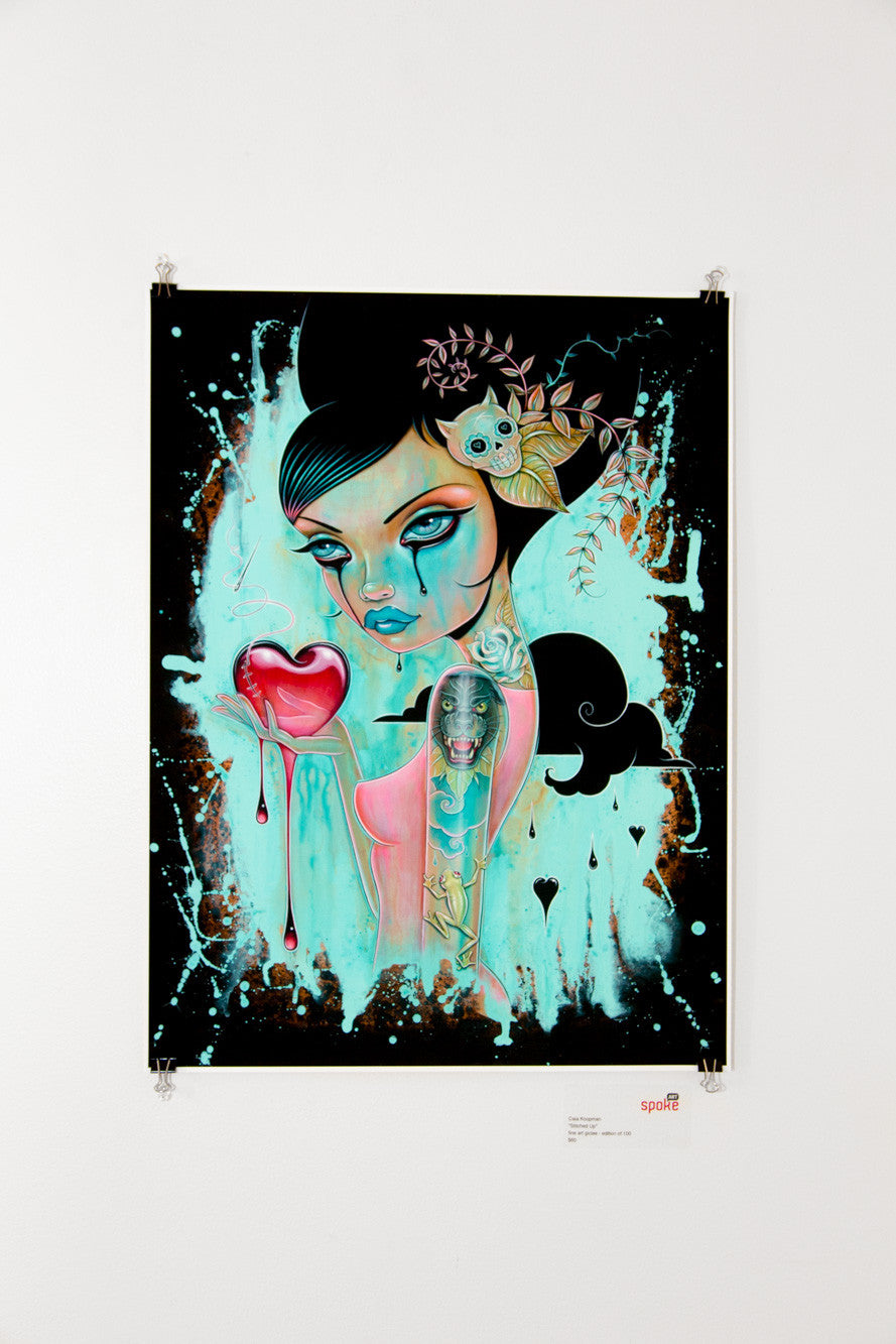 A limited edition artwork by Caia Koopman portrays a stylized woman with large eyes and an intricate hairstyle, holding a dripping red heart. This archival pigment print features abstract designs and muted aqua splashes, creating an ethereal, surreal ambiance.