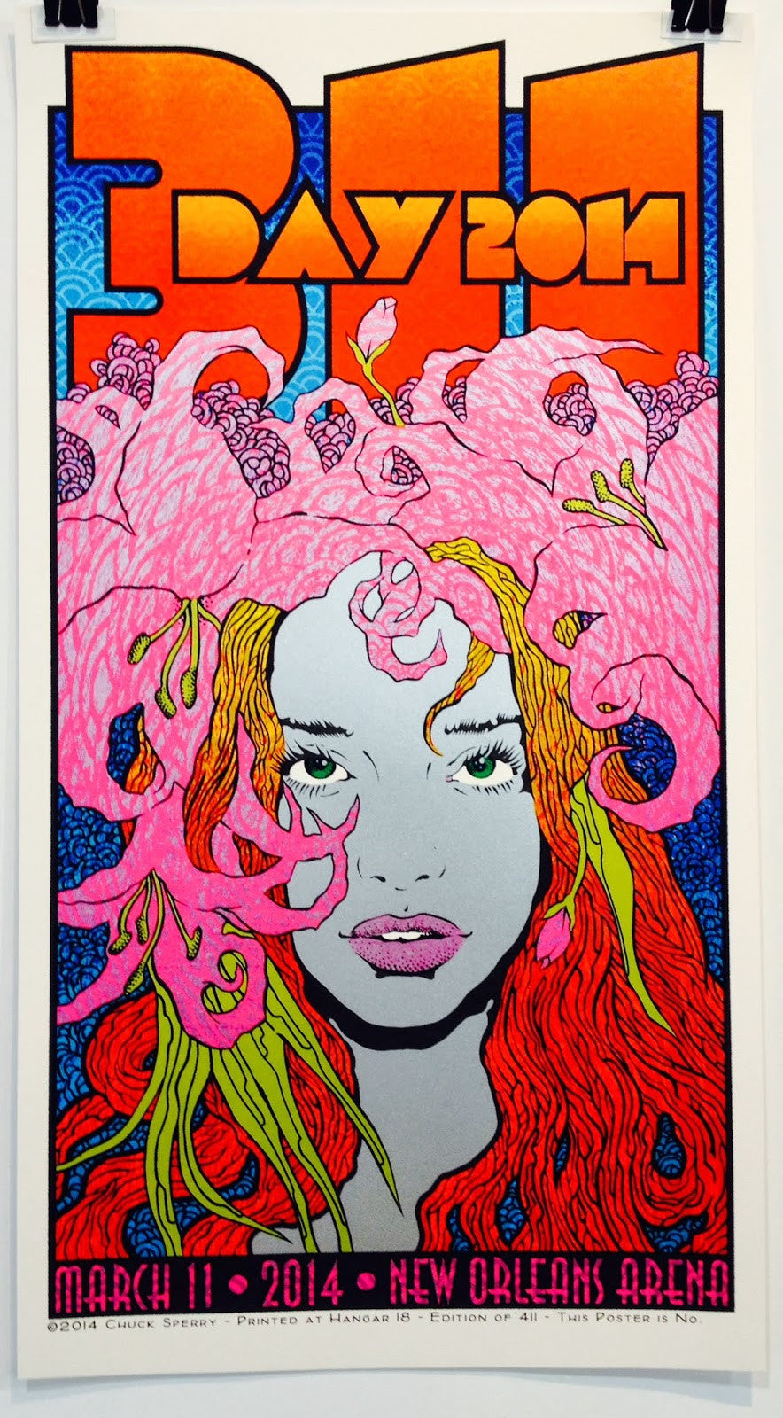 Chuck Sperrys vibrant screenprint poster showcases a womans face with bright red hair and pink flowers, bold text reading 311 Day New Orleans 2014, and event details: March 11, 2014, New Orleans Arena. The design is colorful and psychedelic.