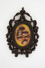 Tatiana Suarezs surreal oil on canvas painting is set in an ornate oval frame. It features a multi-eyed face with dark lashes and yellowish skin. The intricate scrollwork of the dark frame contrasts vividly, capturing the essence of the Through the Veil exhibition.