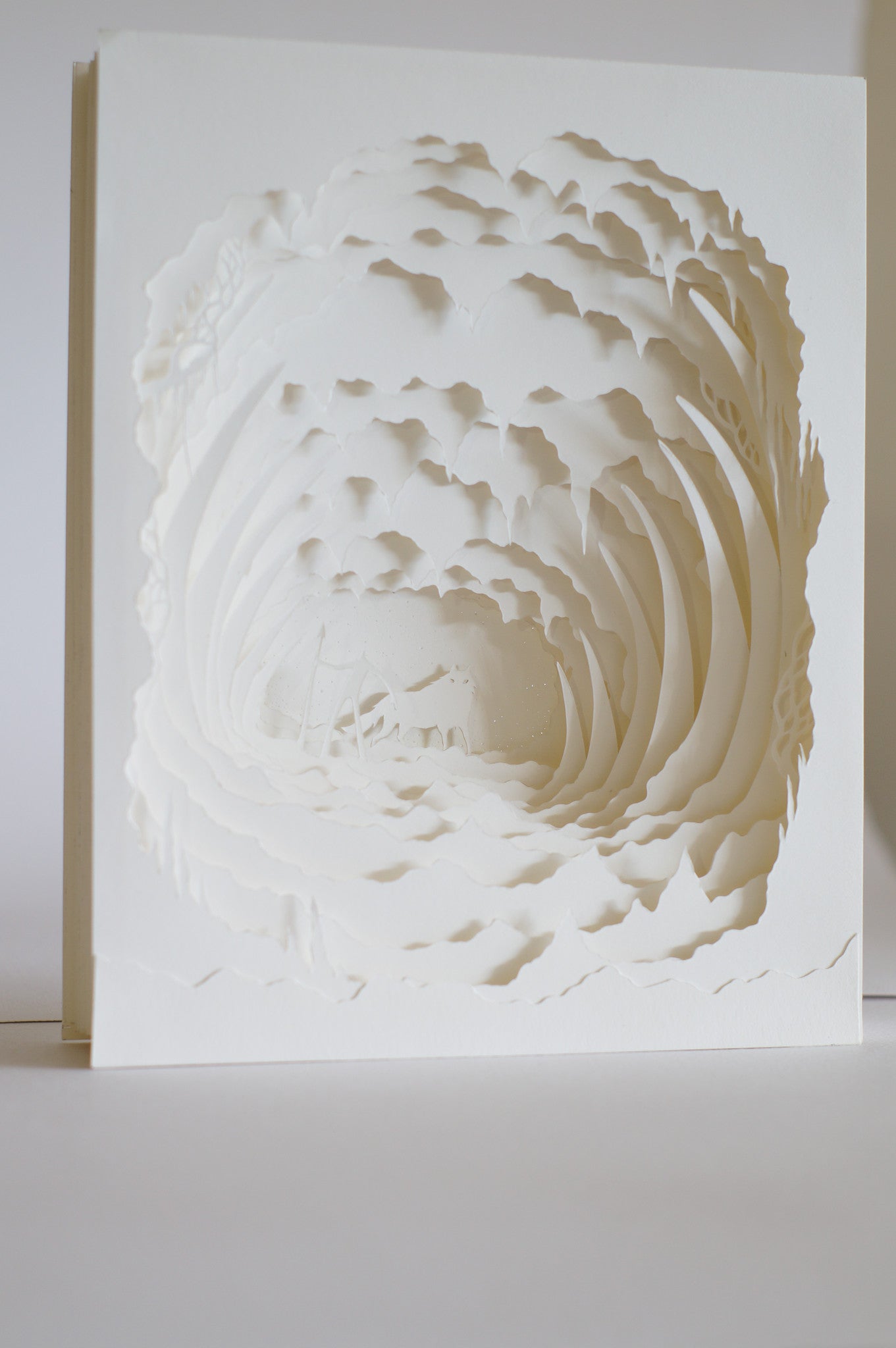 A delicate sculpture by Hari & Deepti features intricately cut white paper layers, creating a tunnel effect. Each layer adds depth and texture, reflecting the enchanting quality of Where the Giants Rest.