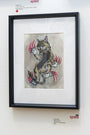 The Cody Miles artwork features a cat with red claws scratching through the canvas, part of the Lil Bub exhibit. Displayed on a wall with artist info labels nearby, this piece uniquely blends creativity and feline charm.