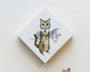 At the Spoke Art exhibit, Lily Piri presents a whimsical painting of a cat astronaut wearing a helmet and suit. The feline stands on its hind legs against stars and a planet on a diamond-shaped canvas displayed on a white wall.