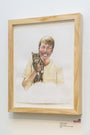 Christine Hostetlers watercolor portrait, framed in wood, captures a smiling person holding Lil Bub amid warm tones. The person wears a light shirt while Lil Bub displays her iconic stripes. This charming piece is part of a San Francisco gallery collection, with a price label below the frame.