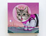 Supersonic Space Princess, a whimsical Arabella Proffer painting, depicts a wide-eyed cat in a spacesuit with a clear helmet and floating crown against a pink alien landscape with planets and spiky mountains, capturing the playful charm of the Lil Bub art exhibit.