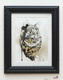 Melanie Alves offers limited-edition framed watercolor prints of a stylized cat with exaggerated eyes and a protruding tongue. The painting has a mostly white background with brown and black splashes, while the textured black frame adds unique detail.