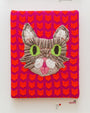 Textile art by Ishknits features a gray and white cat with green eyes and a pink nose on a vibrant red-pink background with a repeating cat pattern, honoring feline icon Lil Bub. Displayed at San Franciscos Spoke Art gallery, its complete with gallery labels nearby.