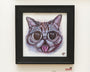 A Joemur framed artwork features a playful, cartoonish cat with large eyes and its tongue out, reminiscent of Lil Bub, drawn in colorful scribbled lines. The black frame reflects Spoke Art style and is signed with the initials HM.