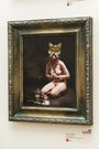 This limited edition Ransom & Mitchell poster showcases a captivating scene: a nude figure in a cat mask kneels with a flower amid a milk bottle, dead bird, and rat. Displayed on white walls, it reflects the vivid imagery and themes of the Lil Bub show.