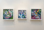 Three vibrant abstract artworks by Crystal Wagner, featuring swirling patterns in pink, blue, green, yellow, and lavender hues, hang on a white wall in white frames. These pieces resemble dynamic screen prints that captivate the viewers eye.