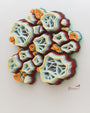 This vibrant 3D artwork by Charles Clary features layered, wavy shapes resembling abstract coral or geological forms. Hand-cut paper in orange, white, and blue adorns a white wall, with the artists signature in the corner.