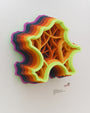 This vibrant wall sculpture by Charles Clary resembles a stylized map with organic shapes. It is crafted from hand-cut paper featuring neon yellow, orange, red, green, and purple concentric outlines. Intricate patterns reveal striking depth against a white background.