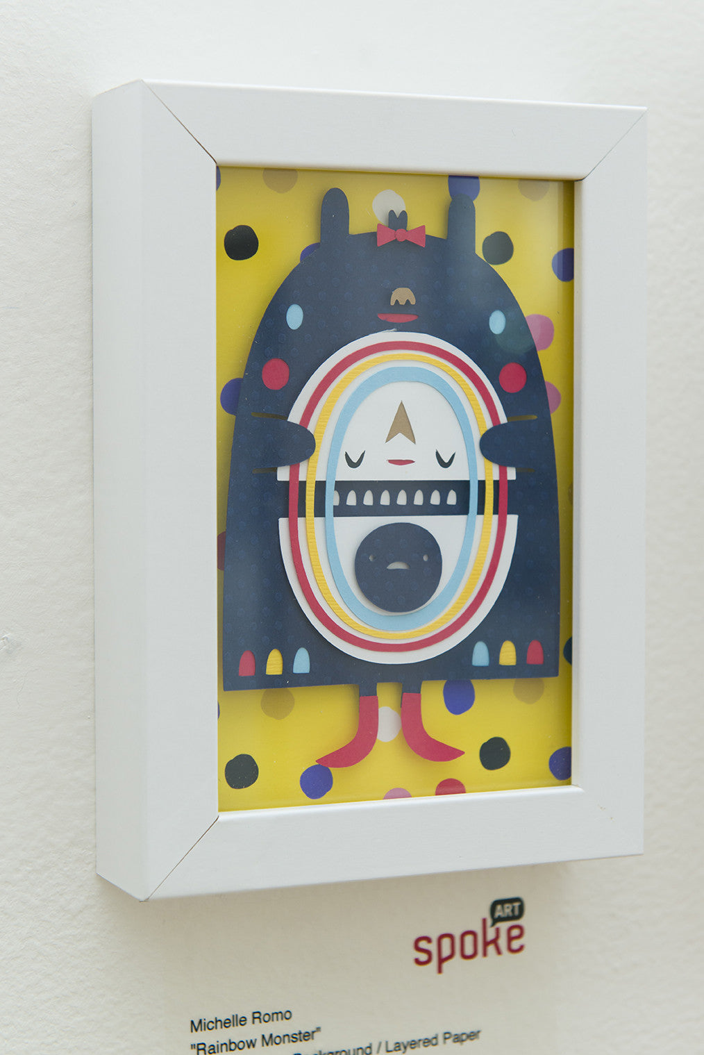 The Rainbow Monster by Michelle Romo from Crowded Teeth shows a whimsical creature with a rainbow face amid colorful polka dots on yellow. Its presented in a white frame, making this giclee print an expressive addition to any gallery wall or space.