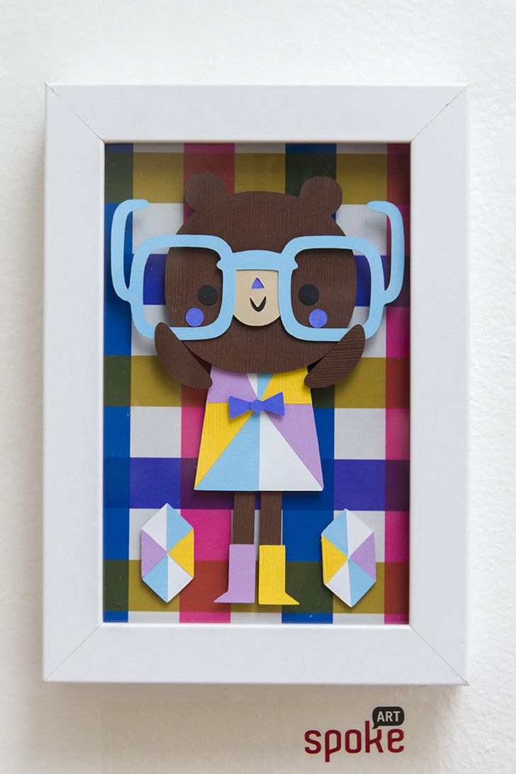 Crowded Teeth offers a framed giclee print of a cartoon lady bear wearing oversized blue glasses and colorful geometric clothes. The vibrant background features a multicolored checkered pattern with the word spoke subtly at the bottom—a true masterpiece.