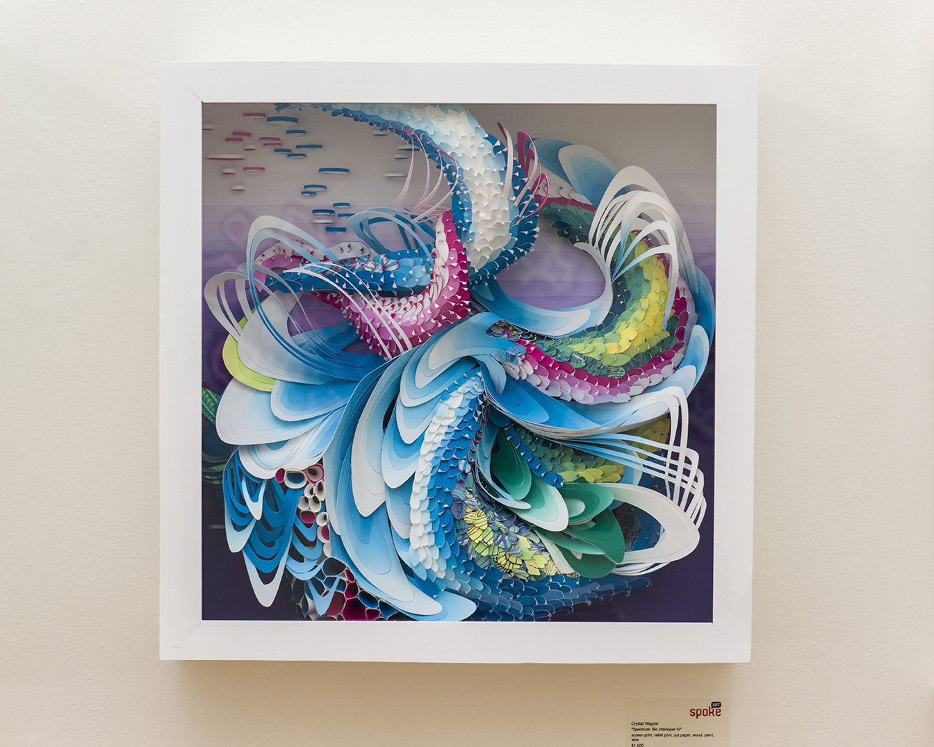 Crystal Wagners abstract art piece features swirling vibrant blues, purples, and greens that flow like waves or feathers. Framed in white, it showcases layered textures on a light background resembling an intricate screen print.