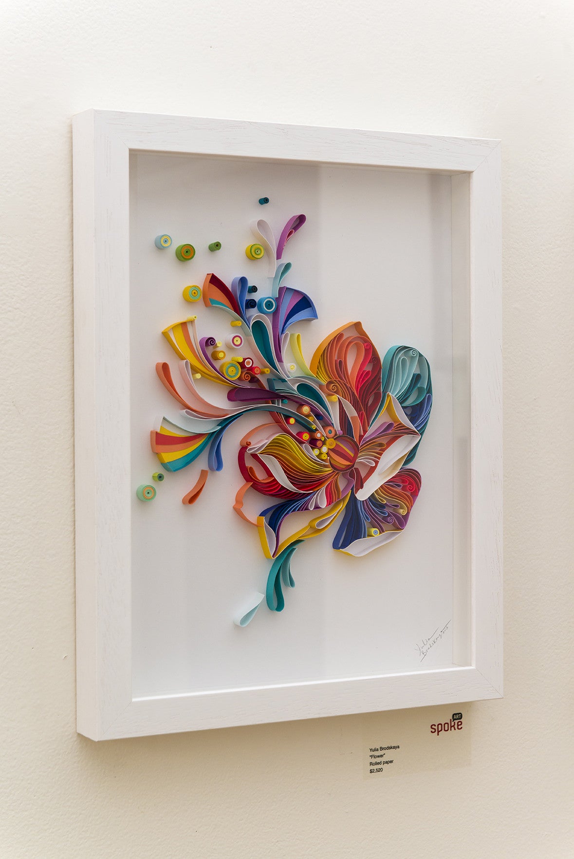 Framed artwork by Yulia Brodskaya features a vibrant abstract flower made of colorful hand-cut quilled paper strips against a light background, labeled SPQR. Its an invitation for art enthusiasts to bring this unique piece home.