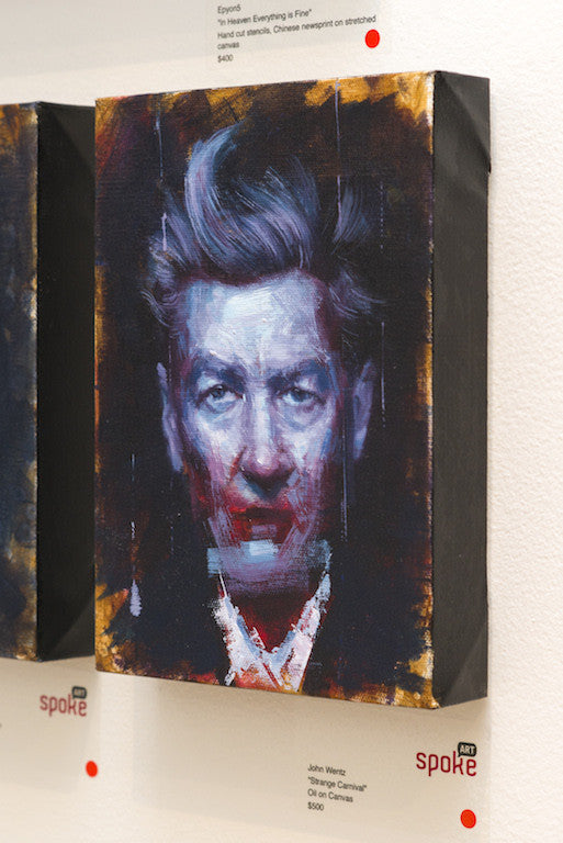 A textured oil painting by John Wentz features a mans face with dramatic, abstract brushstrokes akin to Strange Carnival. The piece has dark-edged canvas and hangs on a gallery wall, with a label below showcasing the artists name and price.