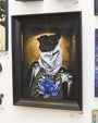 A Joemur painting showcases a shrouded skeleton in a dark garment, adorned with a vivid blue lotus on its chest. Crafted meticulously in oil on canvas, this framed artwork is elegantly displayed on the gallery wall.
