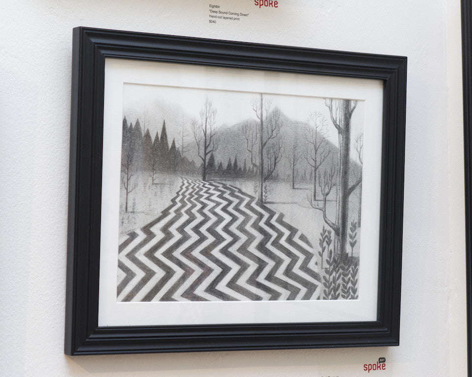 A framed black and white graphite artwork by Ruel Pascual, evoking Twin Peaks, features a zigzag path through a forest with towering trees and mountains. It is displayed on the wall with accompanying gallery tags.
