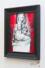 A framed mixed media artwork by Jon Wayshak shows a woman with an animal head in a white dress on a bench, set against a vibrant red background for striking contrast. Available for art purchase on the gallery wall.