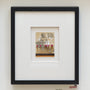 This Jason DAquino artwork showcases a graphite sketch of a seated figure with small vertical pins below, artfully drawn on a found matchbook. Its elegantly framed with a wide white mat and black border for presentation.