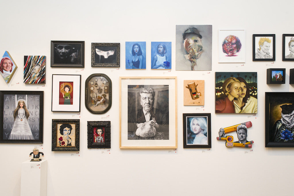 A gallery wall displays an eclectic mix of artworks, including Kate Zambranos portraits and vibrant oil on panel pieces like Alice. The diverse collection features colorful and monochrome elements of varying styles and sizes, all set against a white background.