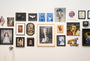 A wall showcases an eclectic mix of framed art, with portraits, abstract pieces, and illustrations in varied styles and sizes. A monochrome oil on canvas by Michael Ramstead featuring a man with a dog takes center stage, suggesting its available for purchase.