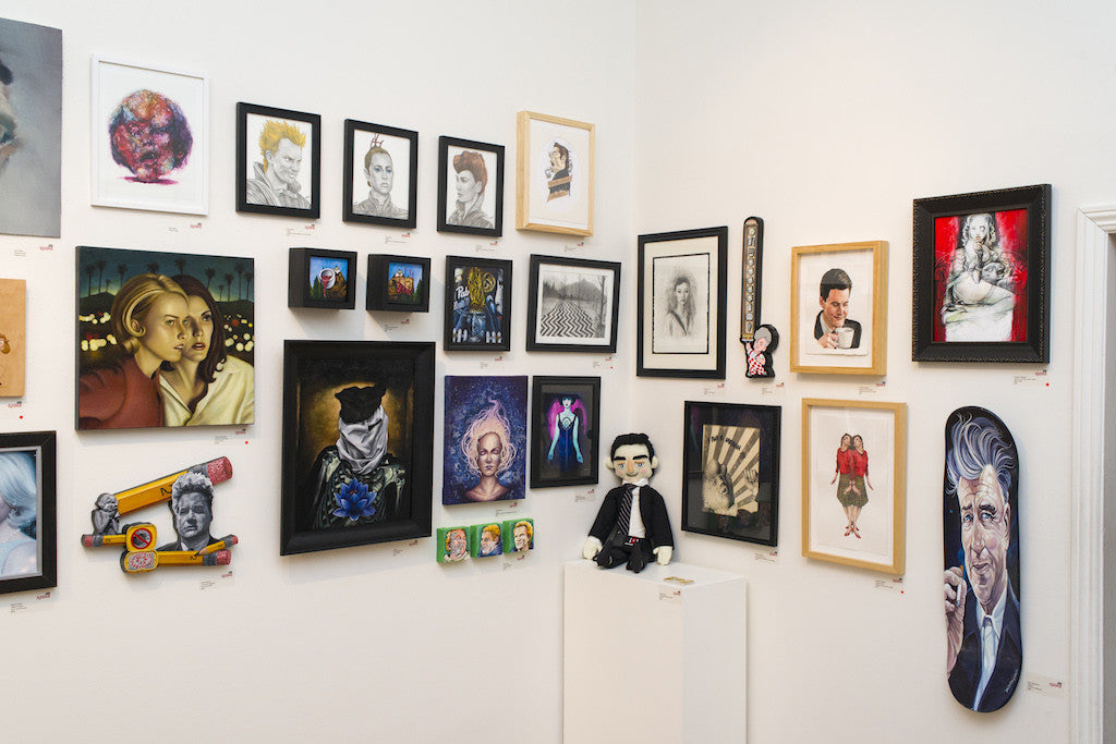 A gallery wall features acrylic portraits, abstract designs, and a skateboarding man, all in bold Geoff Trapp style. In the corner, a black-clad small mannequin rests on a pedestal.