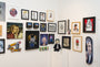 A gallery wall features framed artworks like portraits and abstracts, with a vibrant Joemur acrylic on panel. Nearby, a small seated figure sculpture and a skateboard titled Frank Emerges with a painted face add unique touches to the white space.