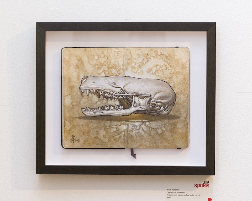 Nate Van Dykes Skull features a Moleskine and Bone drawing of an open-jawed animal skull on a textured sepia background. Its beautifully framed in black and displayed on a white wall.