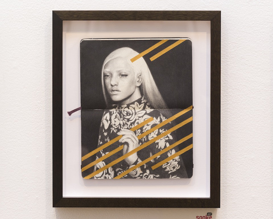 A framed artwork featuring a pencil drawing on a notebook page depicts a person with long hair in a patterned garment. Orange geometric lines, echoing Tran Nguyens style, are overlaid for a contemporary feel.