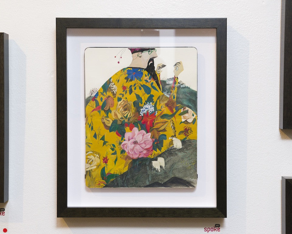 Jon Laus framed artwork showcases a stylized figure with a beard, adorned in a colorful, floral Emperor Gouache-inspired robe. Predominantly yellow, the robe features various flowers. The figure raises a hand against a neutral backdrop, and the black frame adds a touch of elegance.