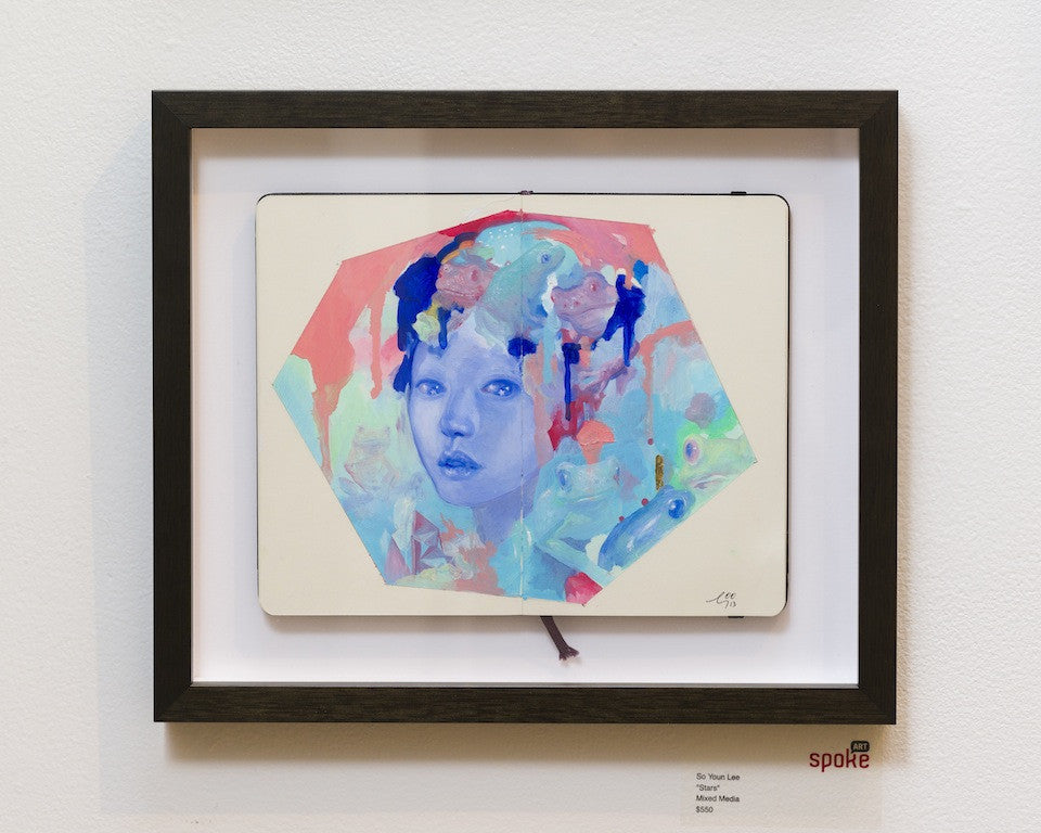 Framed Moleskine artwork Mask by Mei Yan Li, reminiscent of So Youn Lee, showcases a surreal blue-toned face with abstract multicolored shapes in stars mixed media. Its displayed in a gallery for $800.