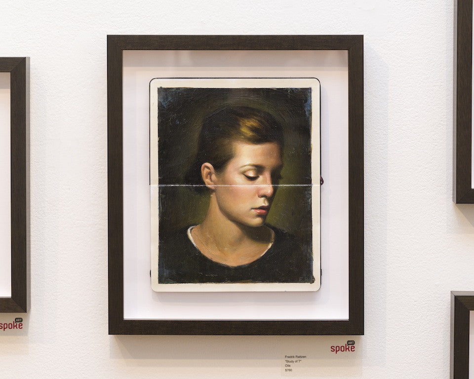 Fredrik Rattzens framed portrait depicts a serene woman with short hair, eyes closed. Crafted in oil on Moleskine, the piece features a unique horizontal fold for added texture and is set in a dark wood frame against a white wall.