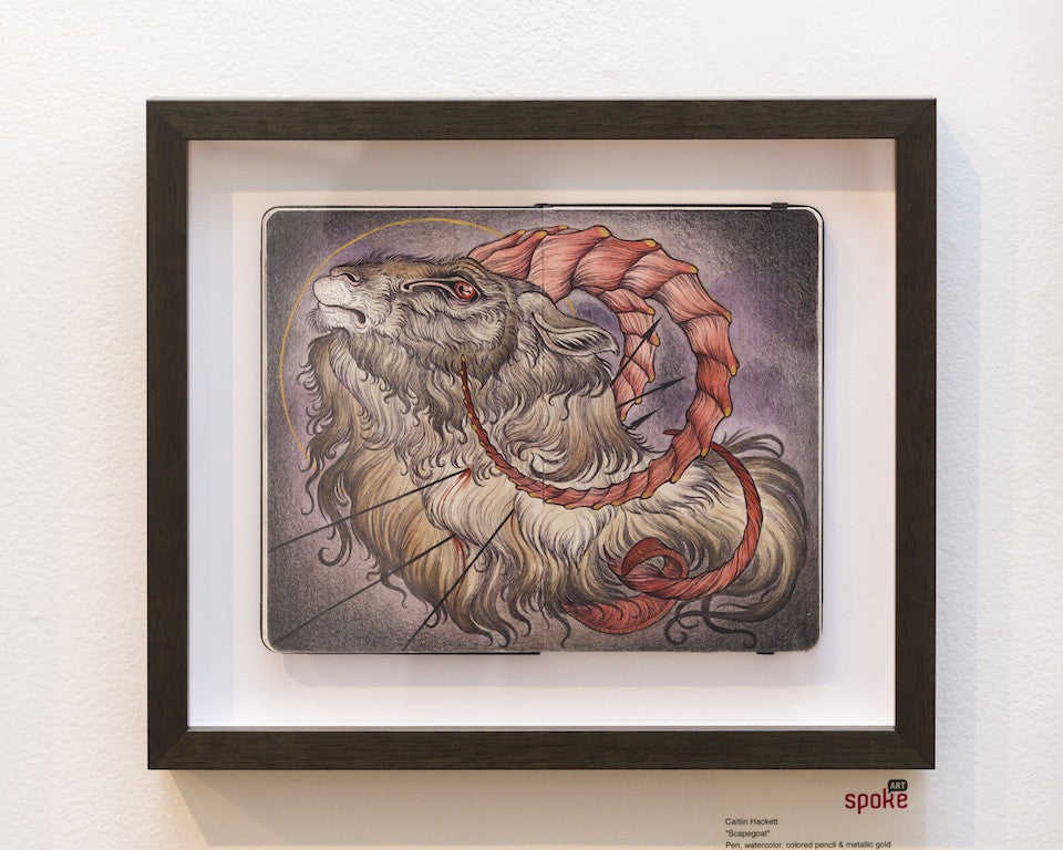 A Caitlin Hackett framed artwork showcases a mystical creature reminiscent of a scapegoat with long, curved red horns, set against a soft gray and purple gradient backdrop, creating an ethereal atmosphere.