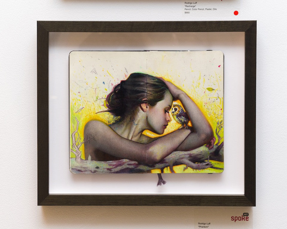 A Rod Luff framed artwork portrays a woman resting her head on her arm, gazing at an owl on a branch. The backdrop resembles a Moleskine page and features yellow and white hues with abstract patterns, evoking a dreamlike atmosphere.
