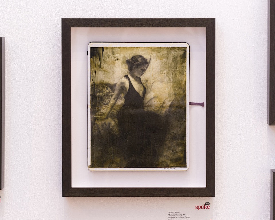 Framed artwork features a woman in a dark dress against an abstract textured backdrop. The sepia tones echo vintage charm, like Tintype Drawing #4, and the black frame with white mat enhances its appeal. It evokes Jeremy Manns atmospheric style on a white wall.