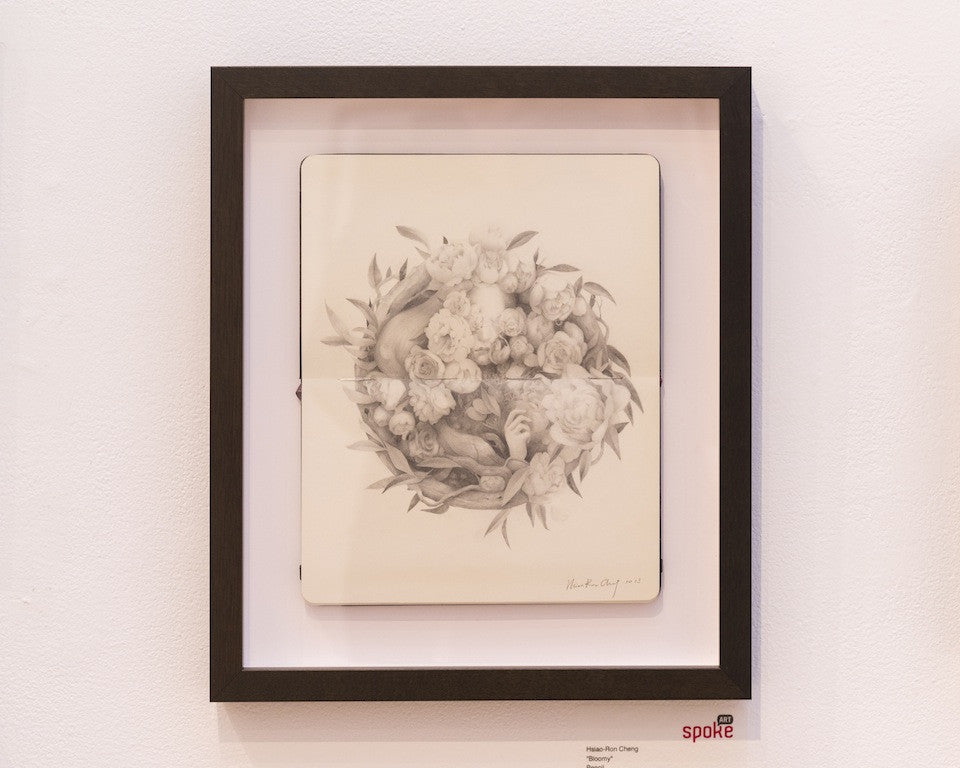This framed piece by Hsiao Ron Cheng showcases a detailed pencil sketch of intertwining snakes and roses. Created on Moleskine, this monochrome artwork is signed by the artist and displayed against a white gallery wall.