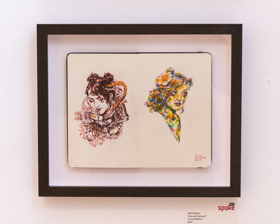 A framed open notebook by Ville Ericsson showcases two vibrant sketches of women, one with a violin and the other adorned with flowers in her hair, capturing the introvert-extrovert art style.