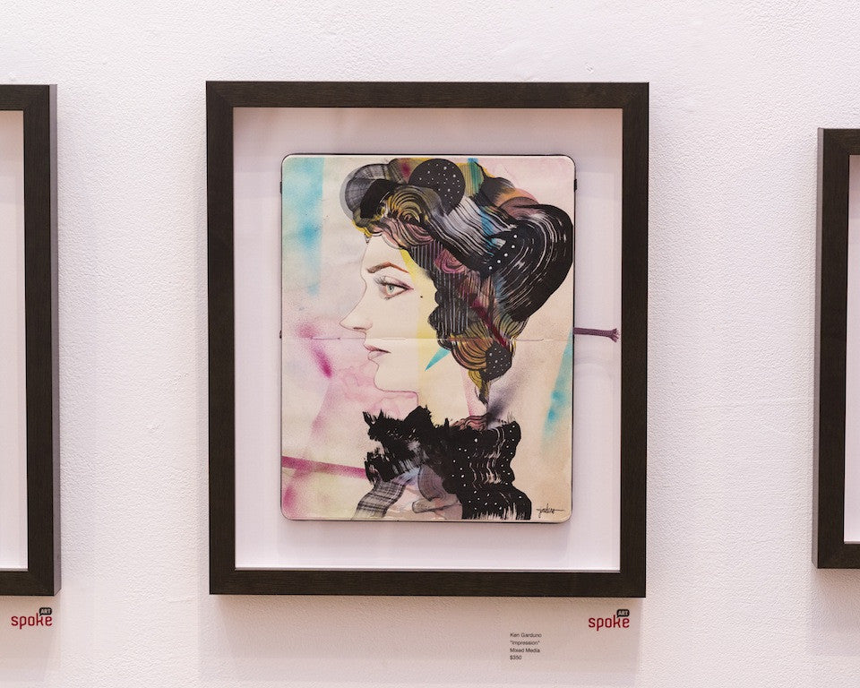 Ken Gardunos mixed media artwork features a woman in profile, blending modern and classical styles with colorful abstract elements. It has bold outlines, vibrant colors, and is displayed in a black frame against a white wall.