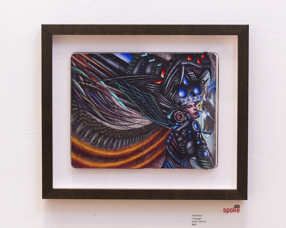 This dynamic framed artwork by Erik Siador features a futuristic figure combining human and machine elements in vibrant acrylic and ink. The abstract composition is set against a white wall in a black frame.