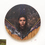 Gene Guynns circular oil painting on wood features a young girl with braided hair emerging from rocky terrain, set against a starry sky intersected by colorful lines, creating a surreal and ornate atmosphere.