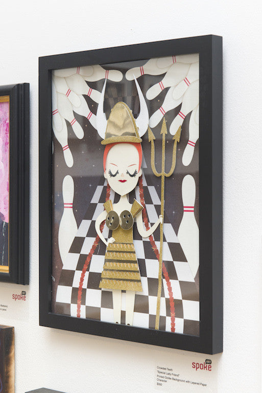 A framed Giclée print by Crowded Teeth showcases a stylized red-haired figure in gold armor with a trident, against bowling pins and a checkerboard background. Displayed in black frame on a gallery wall among other captivating artworks.