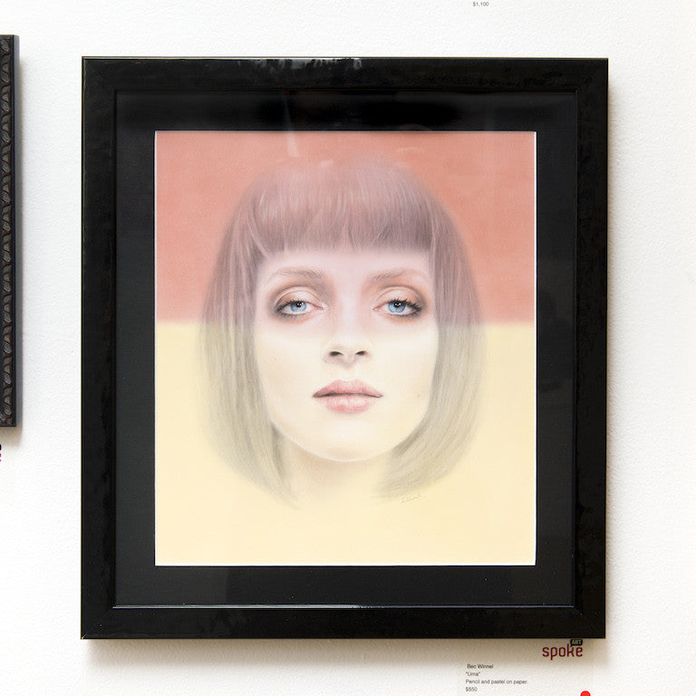 Bec Winnels framed artwork Uma features a surreal portrait of a short-haired woman, drawn with pencil and pastel on paper. The background is peach above and pale yellow below, while her eyes exude a soft, dreamy expression.