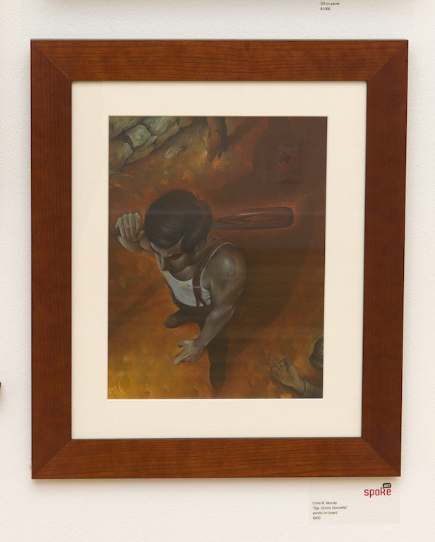 This acrylic on board painting by Chris B. Murray at Spoke Art Gallery shows a man in an undershirt with a tattoo, resembling Sgt. Donny Donowitz. Viewed from above, he grips a knife and stands over another figure on the ground, elegantly framed in wood.