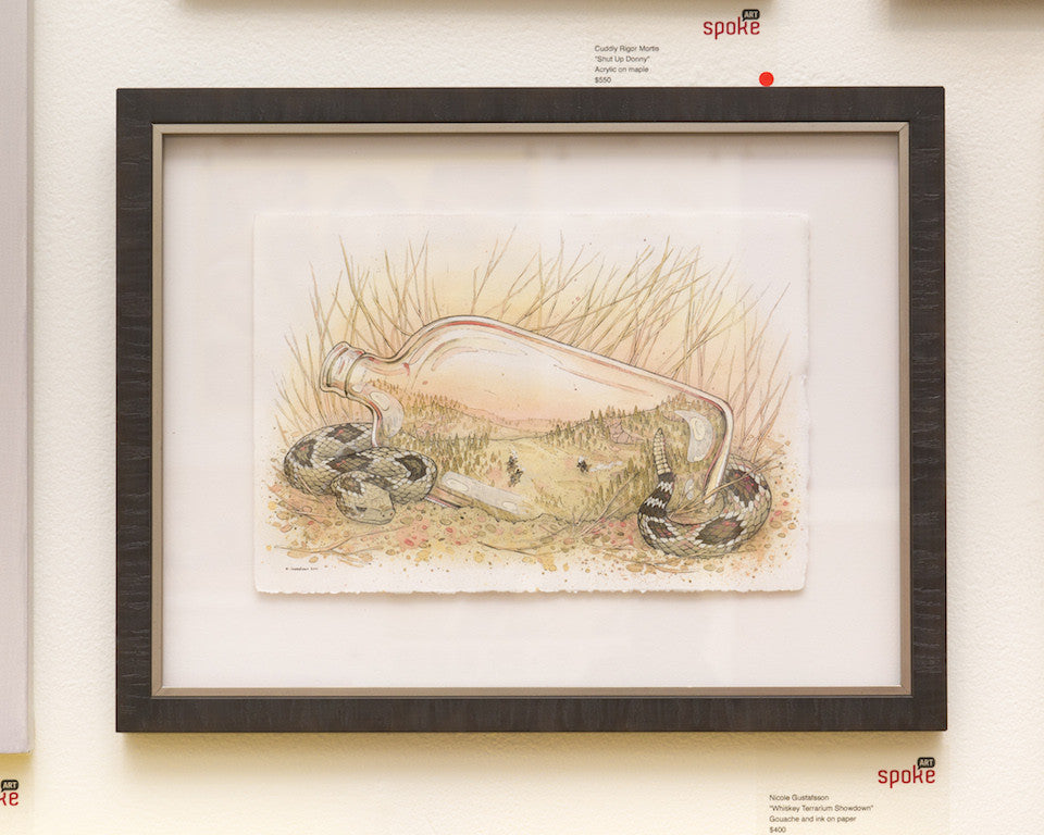 Nicole Gustafssons framed artwork features a transparent bottle in grass filled with intricate illustrations, flanked by two coiled snakes. Created using gouache and ink, the piece uses earthy tones to evoke a natural scene reminiscent of a Whiskey Terrarium Showdown.